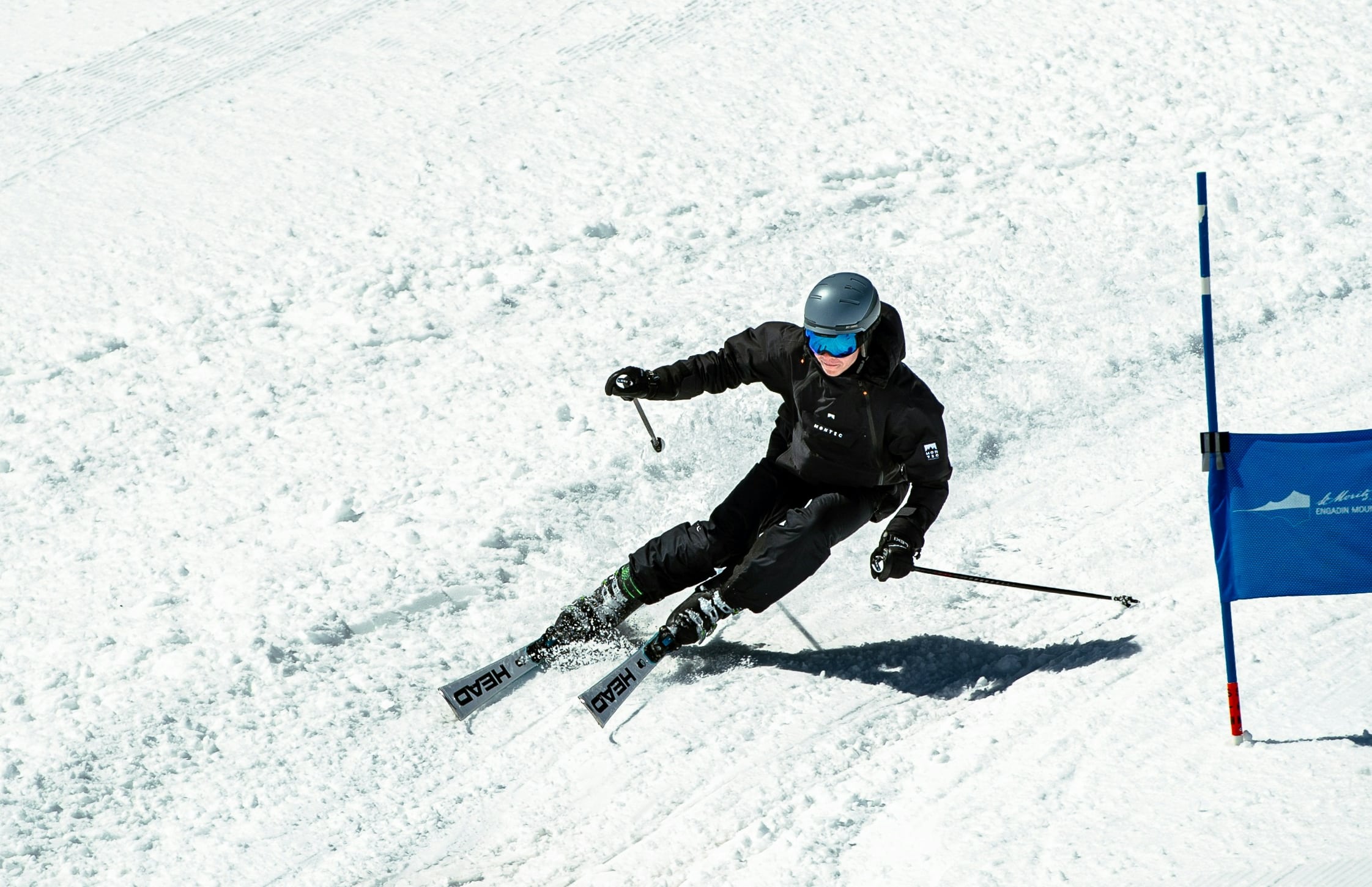 A ski racer carves a tight turn past a blue slalom gate, snow spraying from the edges.